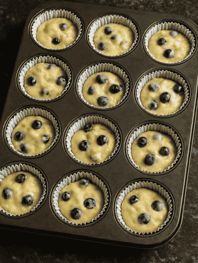 Muffin batter portioned into a 12-cup tin with visible blueberries