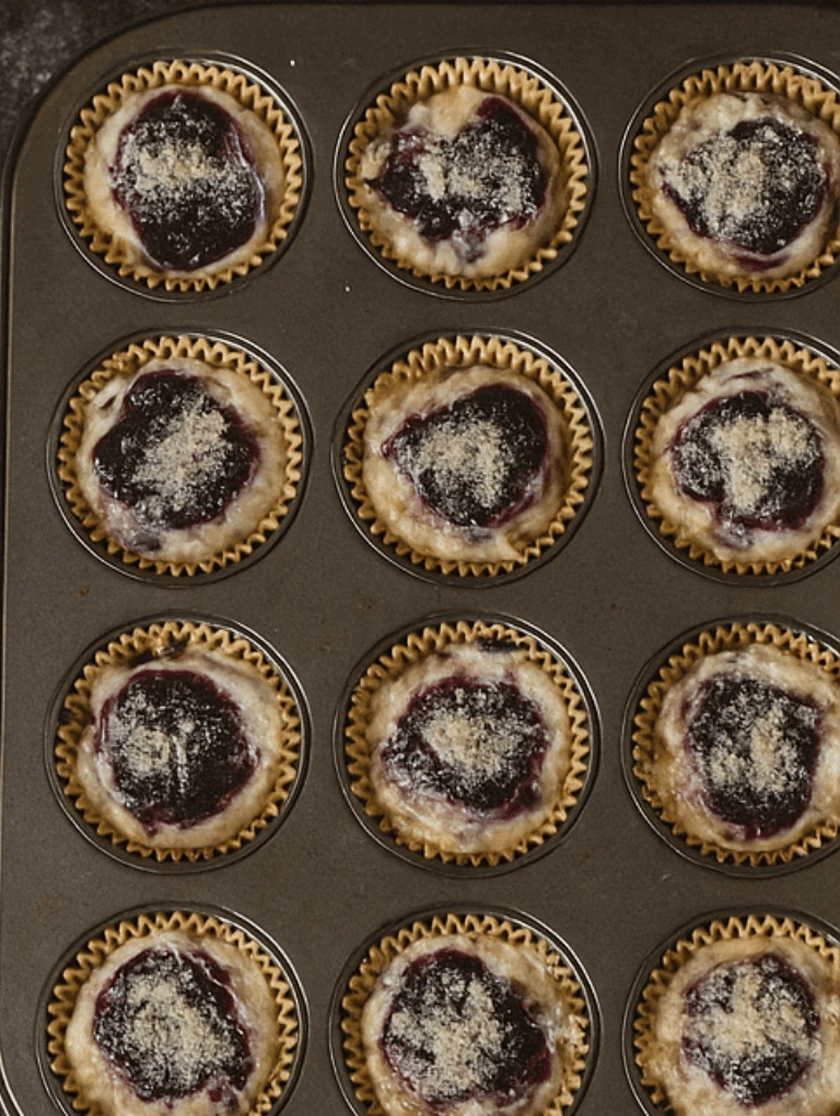 Muffin tin filled with batter topped with blueberry swirl and lemon sugar.
