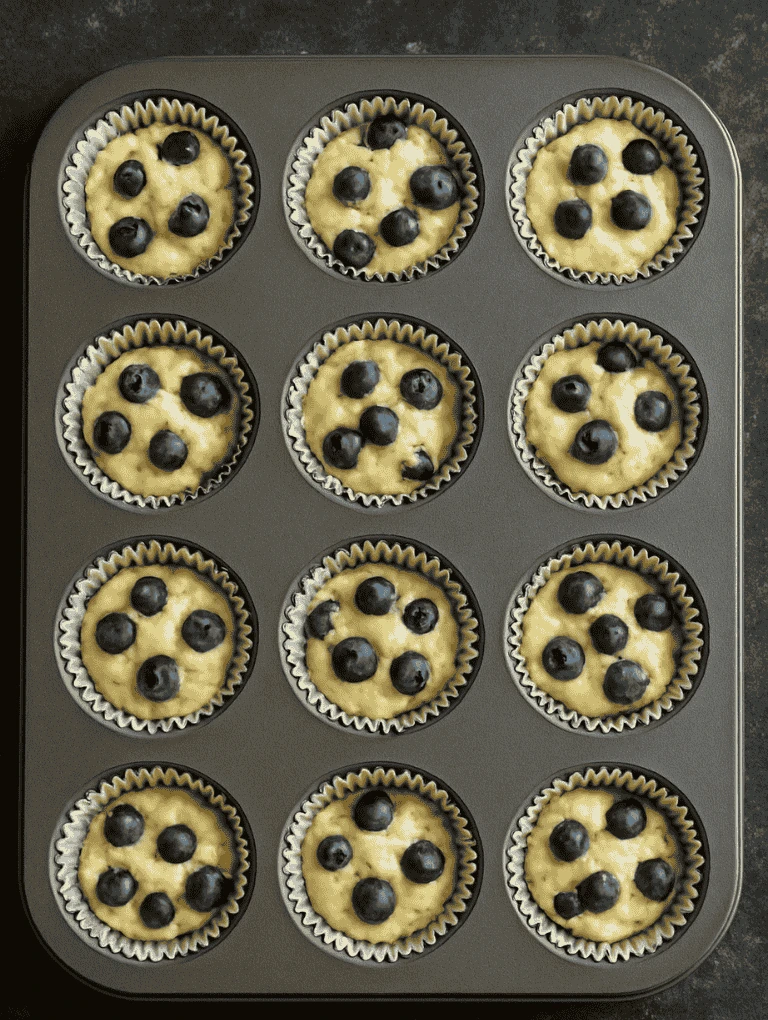 Muffin batter divided into 12 lined muffin cups in a baking tin, ready to bake.