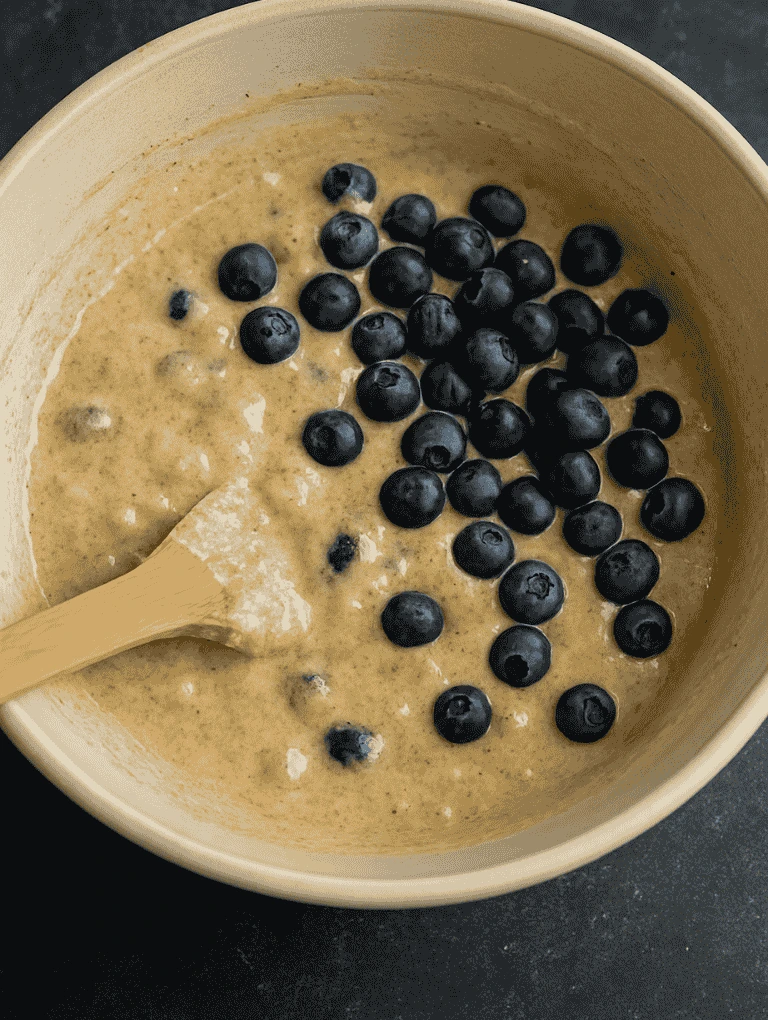 Fresh blueberries and ground cinnamon added to muffin batter in a bowl
