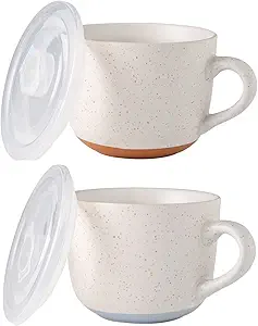 Two speckled ceramic cups with handles, each paired with a transparent plastic lid, one with a terracotta-colored base and the other with a light blue base.
