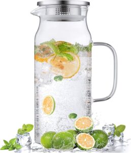 Clear glass pitcher filled with lemon slices, mint leaves, ice cubes, and sparkling water, with fresh limes at the base.