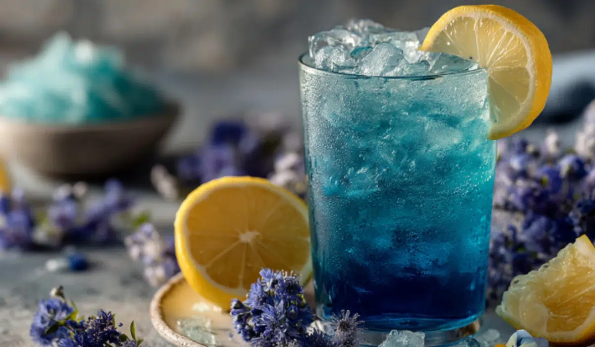 Blue Salt Trick Recipe for Hydration and Weight Loss Clear glass of Persian blue salt water with lemon slice on gray kitchen countertop.