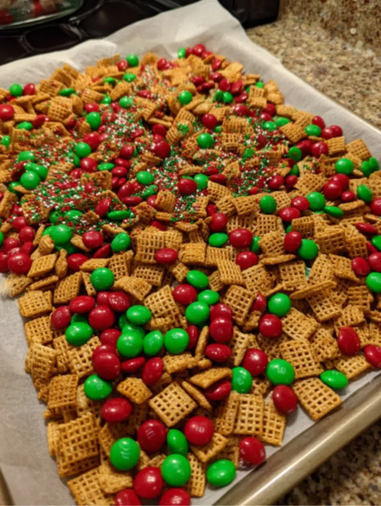 Bowl of Christmas Chex Mix served on the kitchen counter beside mugs of hot cocoa and candy canes, ready to enjoy.