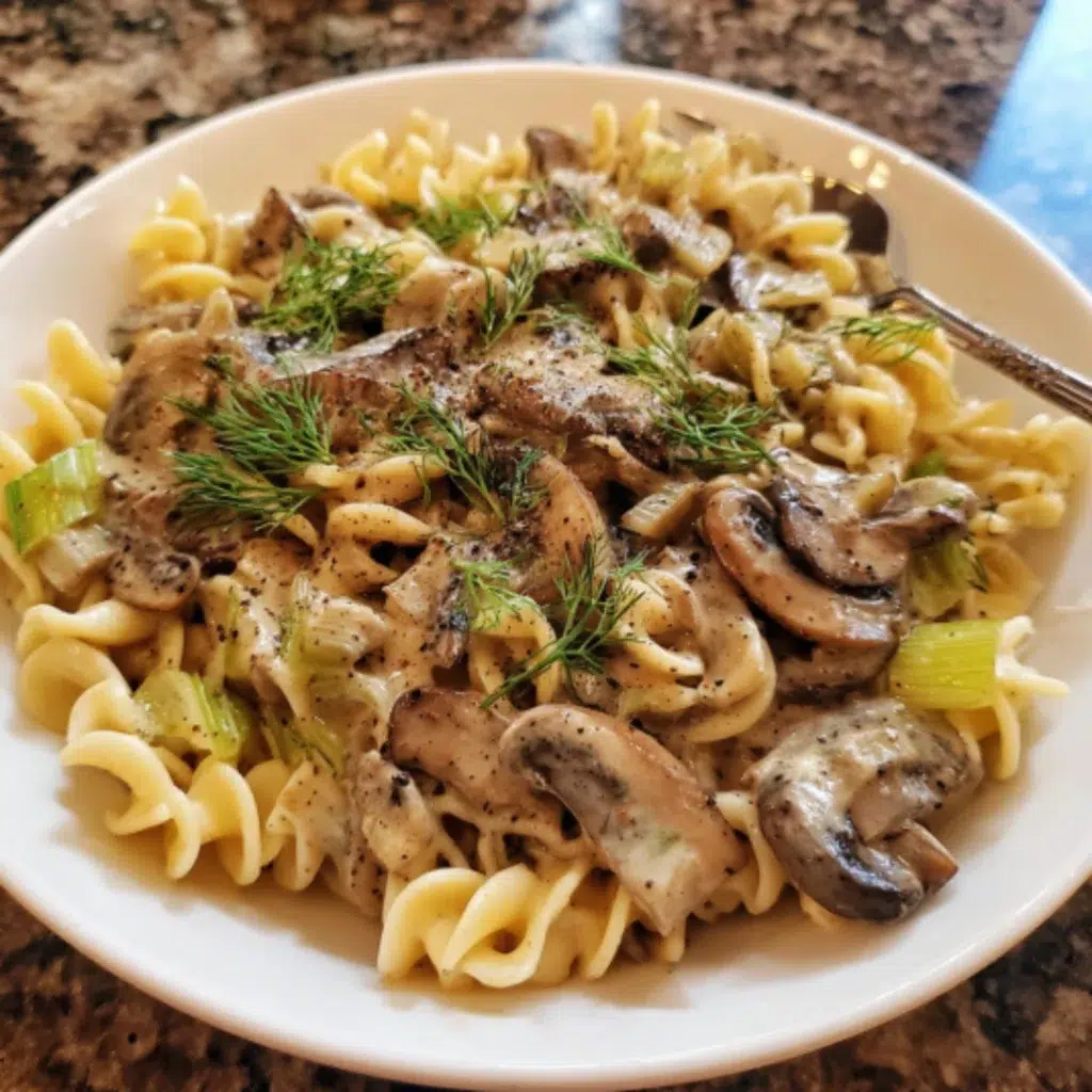 A bowl of creamy vegan mushroom stroganoff topped with crispy mushrooms and fresh dill, ready to serve on a gray kitchen countertop.