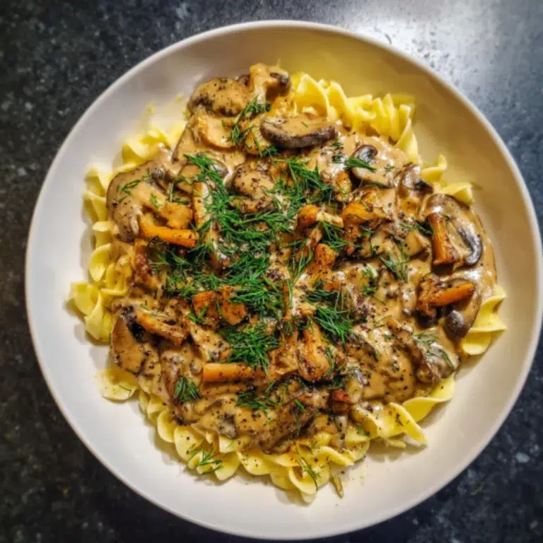 Creamy vegan mushroom stroganoff served on a white plate with golden seared mushrooms and fresh dill on a gray kitchen countertop.