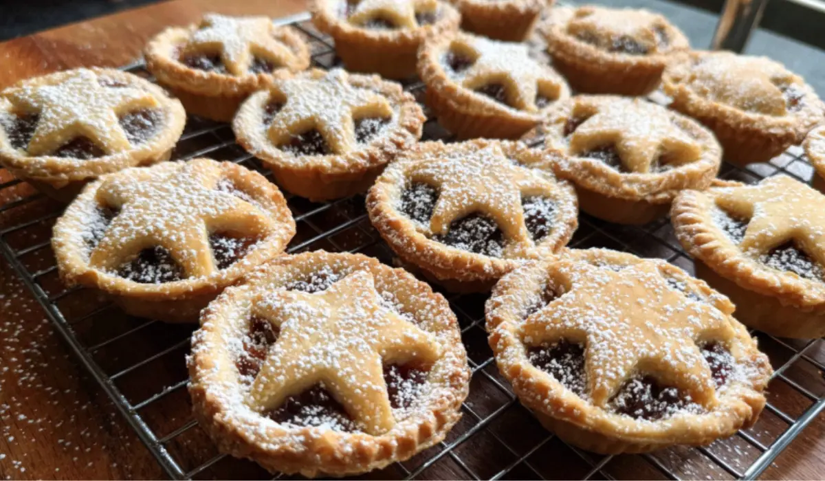 Freshly baked mince pies arranged neatly on a kitchen counter, dusted with powdered sugar in warm holiday lighting.
