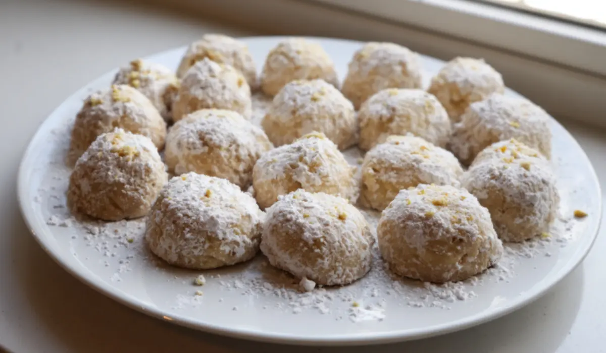 Flat lay of freshly baked snowball cookies dusted with powdered sugar on a kitchen counter, photographed with an iPhone 15 Pro in natural light.
