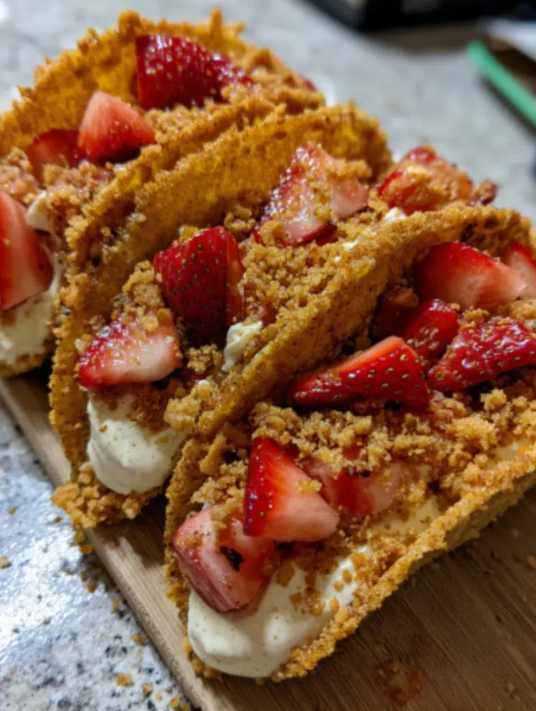 Strawberry Crunch Cheesecake Tacos neatly arranged on a kitchen counter, topped with strawberries and graham almond crumble.