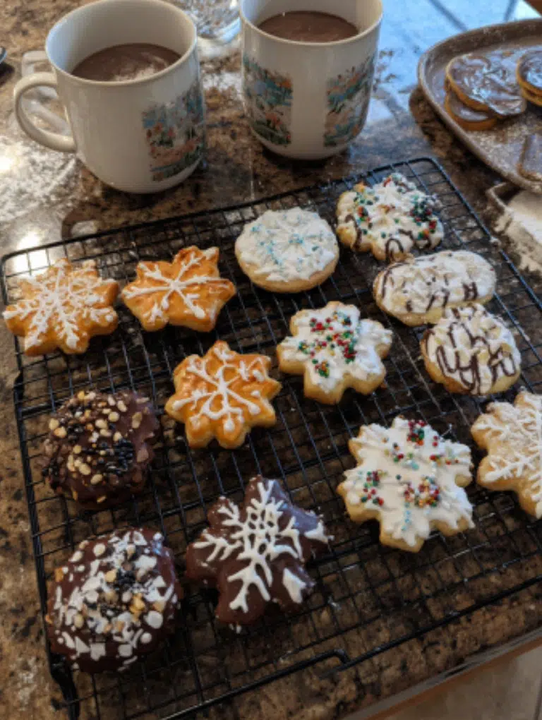 Decorated Christmas sugar cookies with royal icing and sprinkles on a cooling rack.