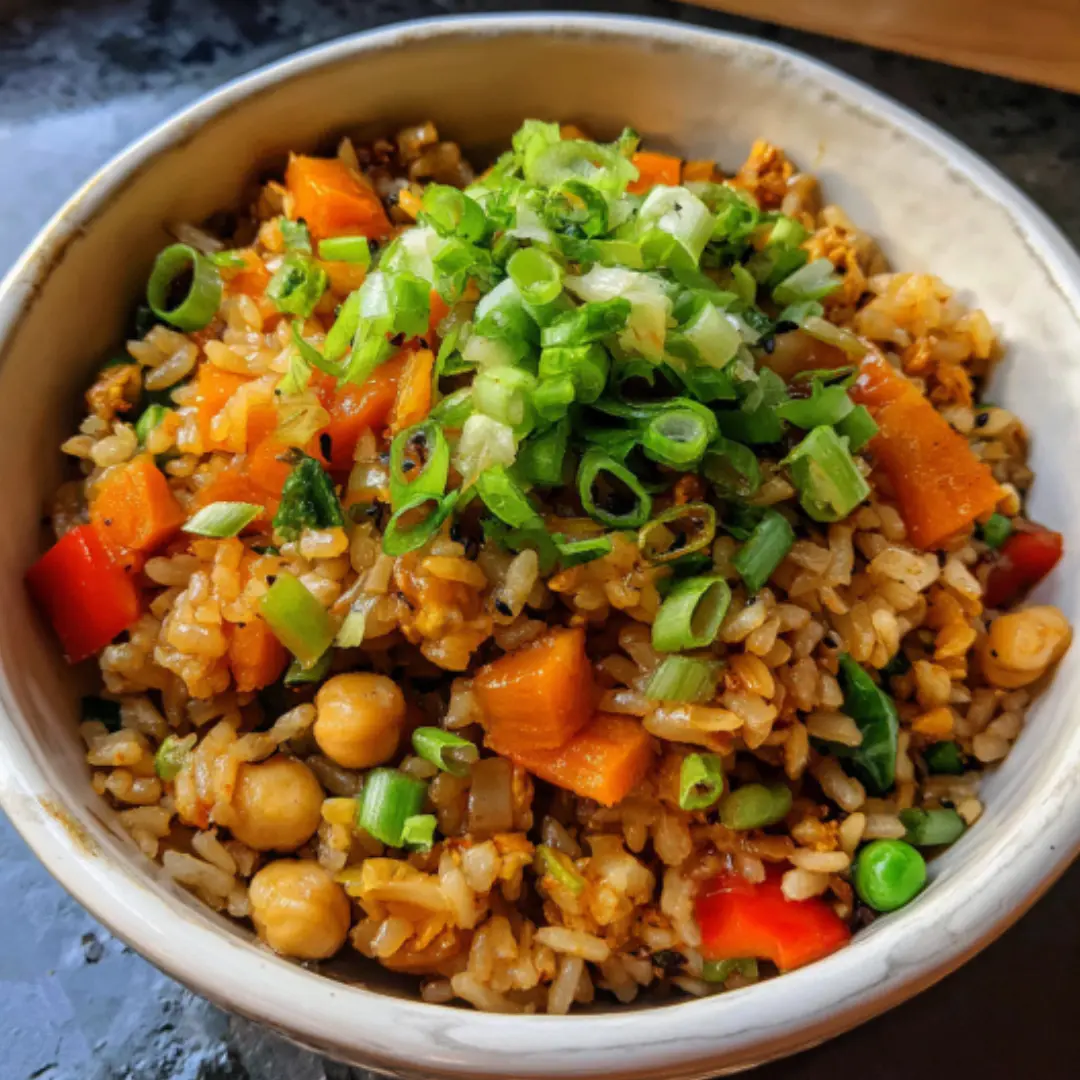 A serving of vegan fried rice in a bowl with a spoon, garnished with green onions.
