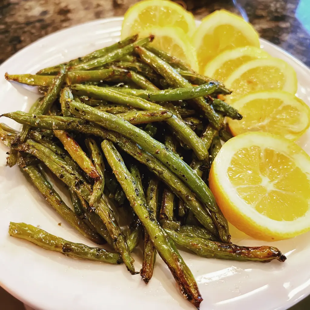 Close-up of perfectly cooked air fryer green beans garnished with fresh lemon on a white plate.